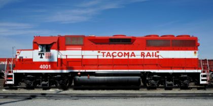 A side view of a red Tacoma Rail locomotive with the number "4001" and white lettering on its body, set against a blue sky.