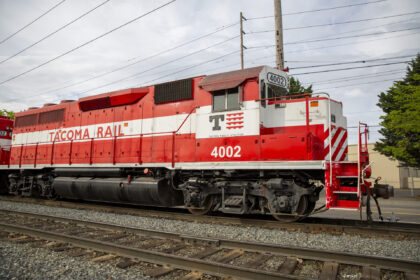 A red and white Tacoma Rail locomotive numbered 4002 is parked on tracks, featuring a front cab with windows and the company name displayed prominently.